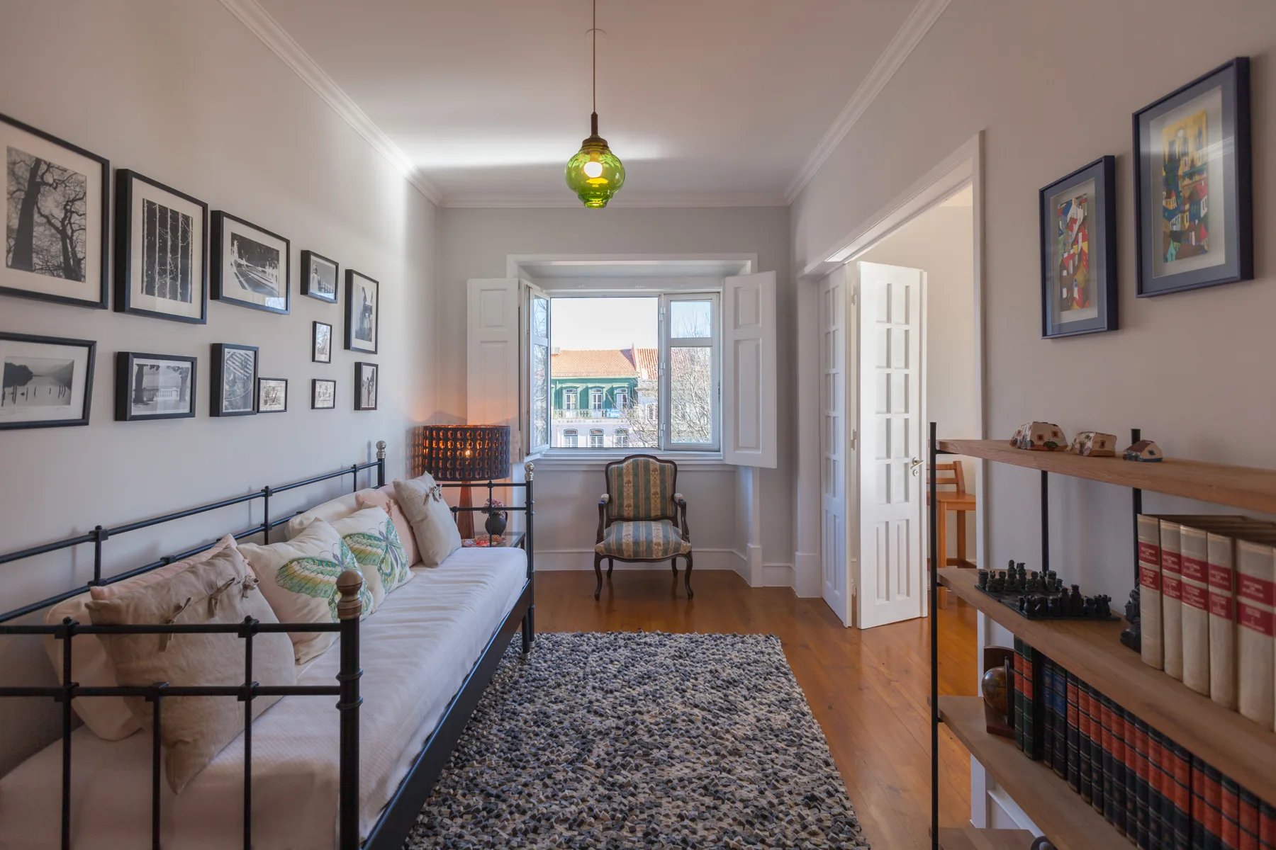A bright living room with a daybed, patterned rug, and a window overlooking nearby rooftops.