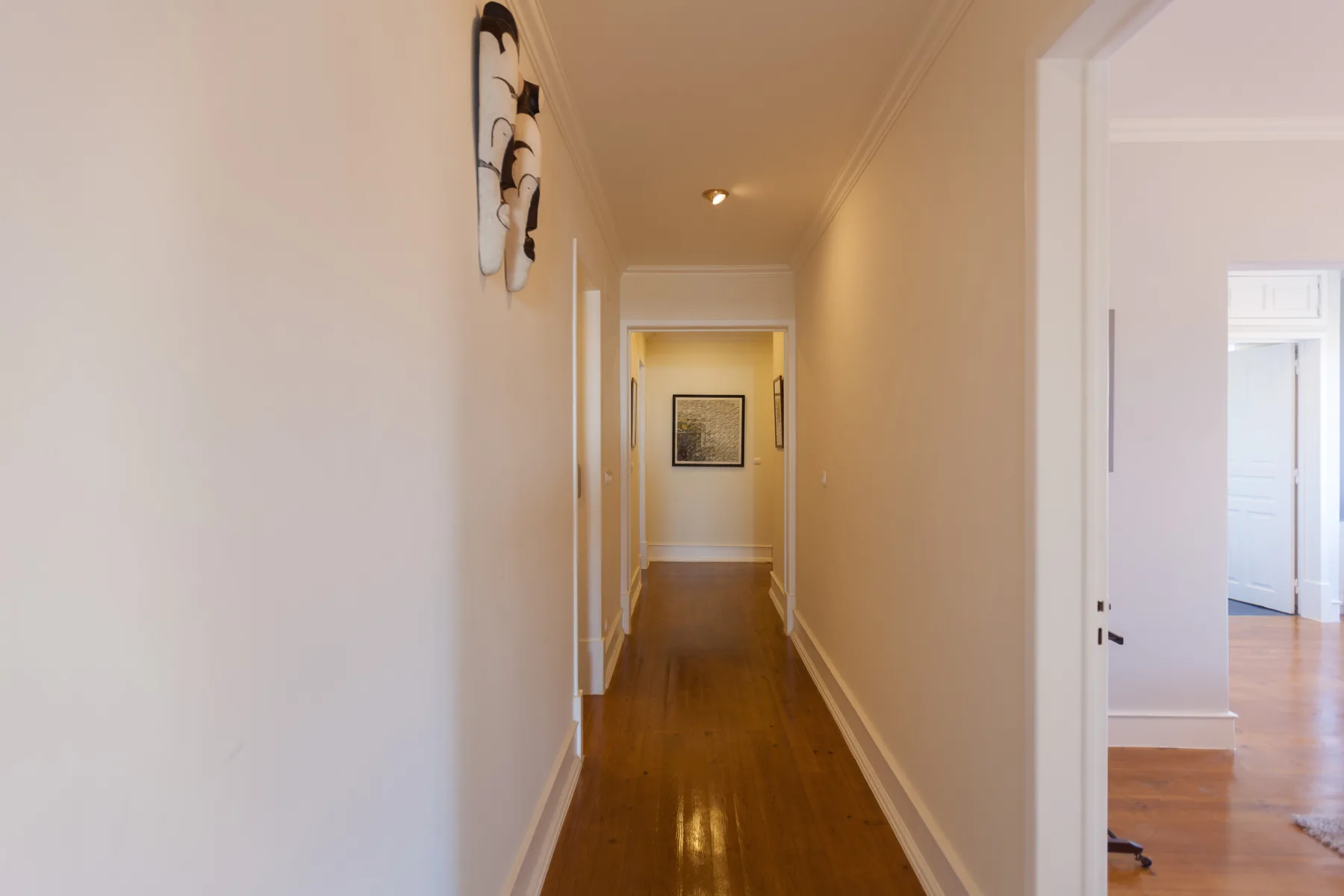 A narrow hallway with polished wood flooring and framed artwork.