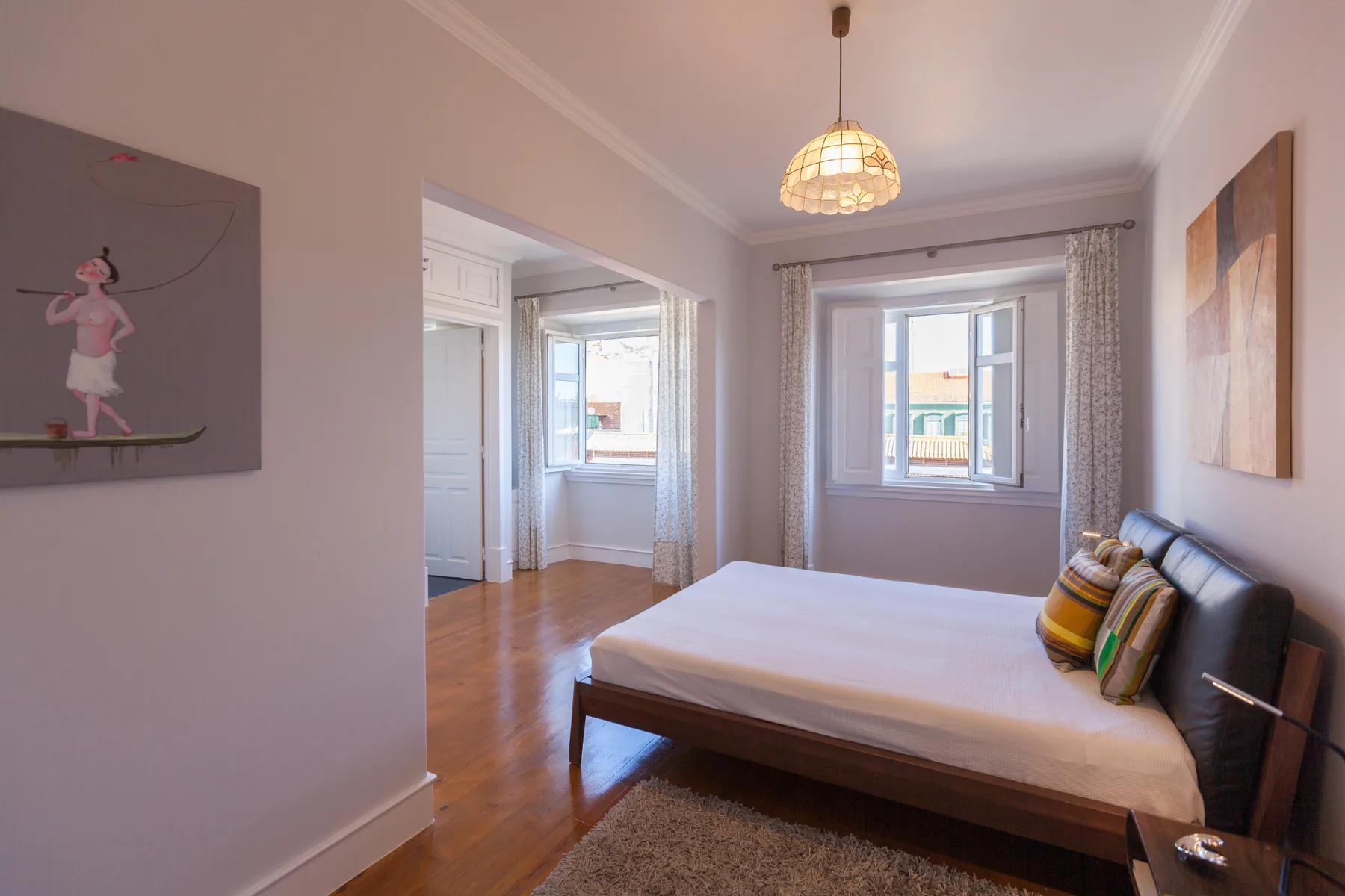 A bedroom with a bed, colorful pillows, and windows opening onto a balcony.