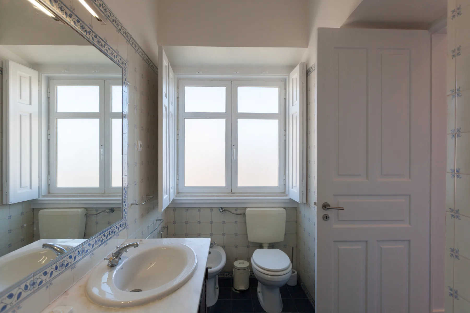 A bathroom with a sink and toilet beside a large window.