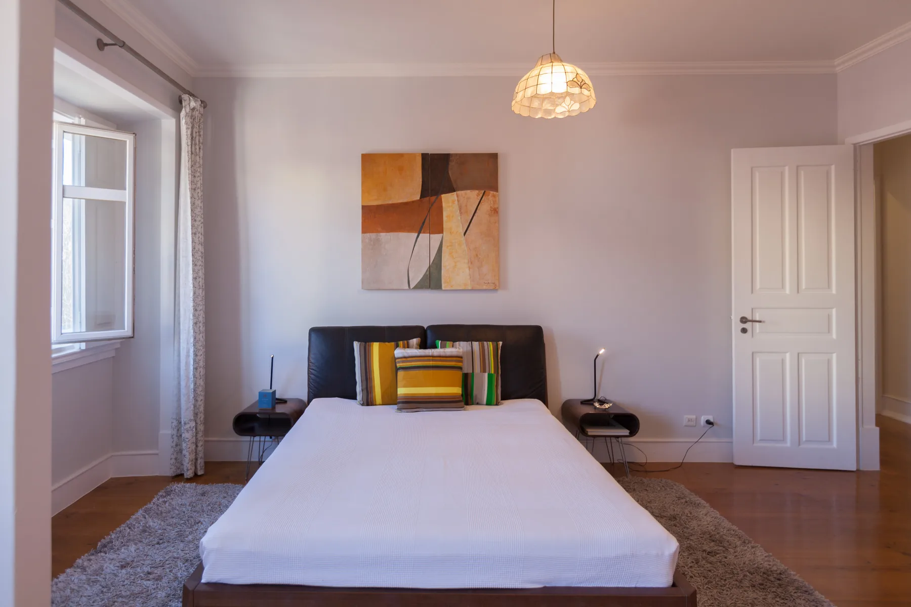 A bedroom with a bed, bedside tables, and abstract artwork on the wall.