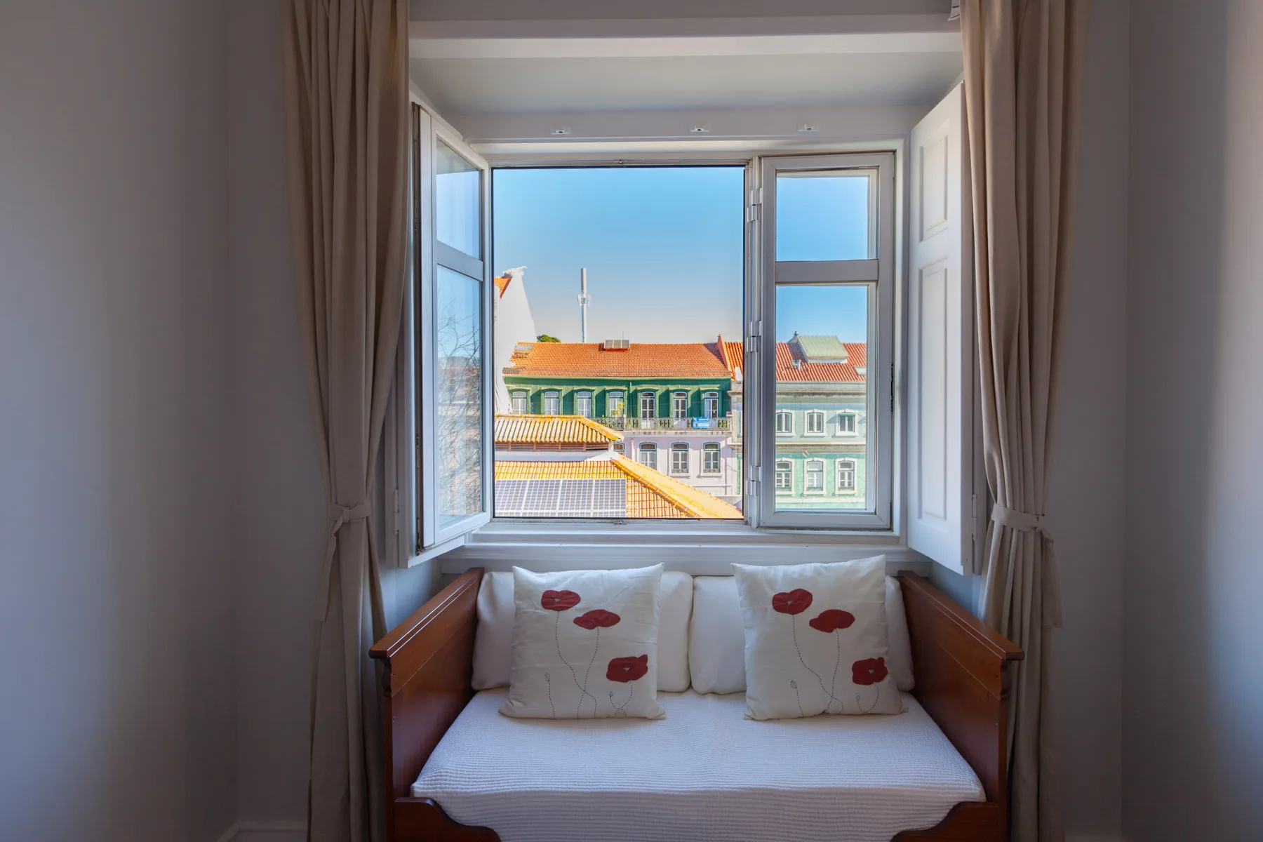A window alcove has cushioned seating and a view of nearby rooftops.