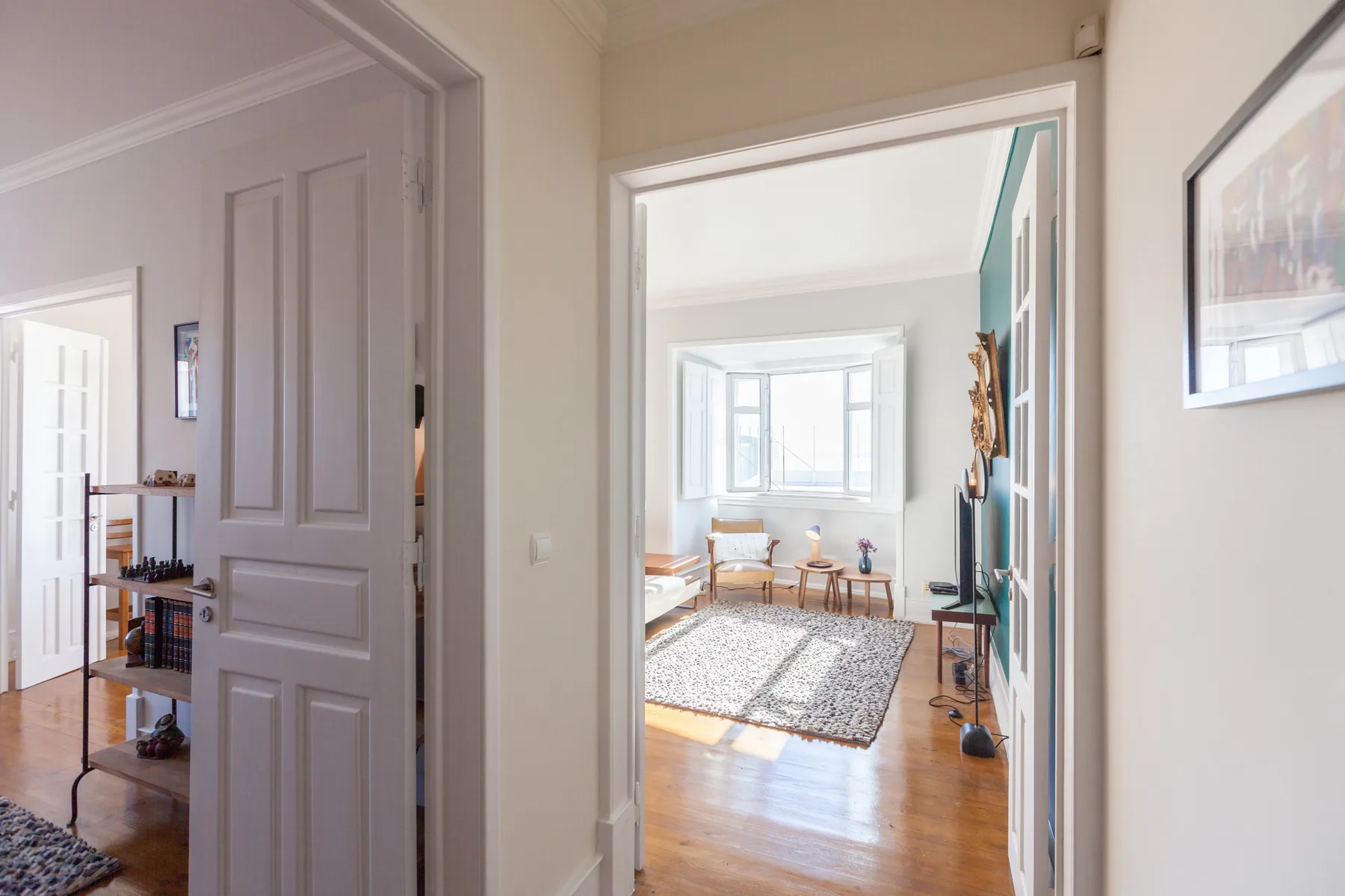 A bright apartment hallway opens onto a sitting room with a rug and large windows.