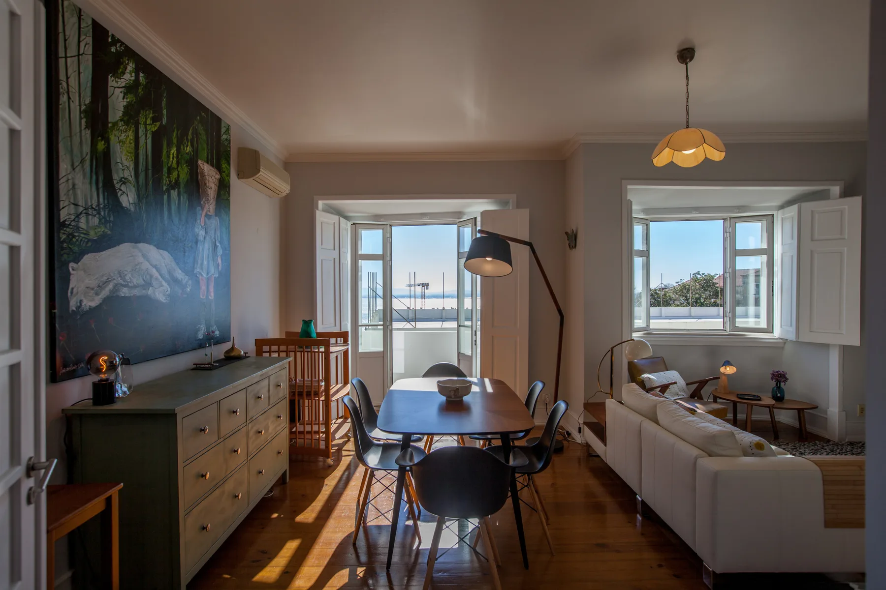 A bright living and dining room with seating, a table, and open windows.