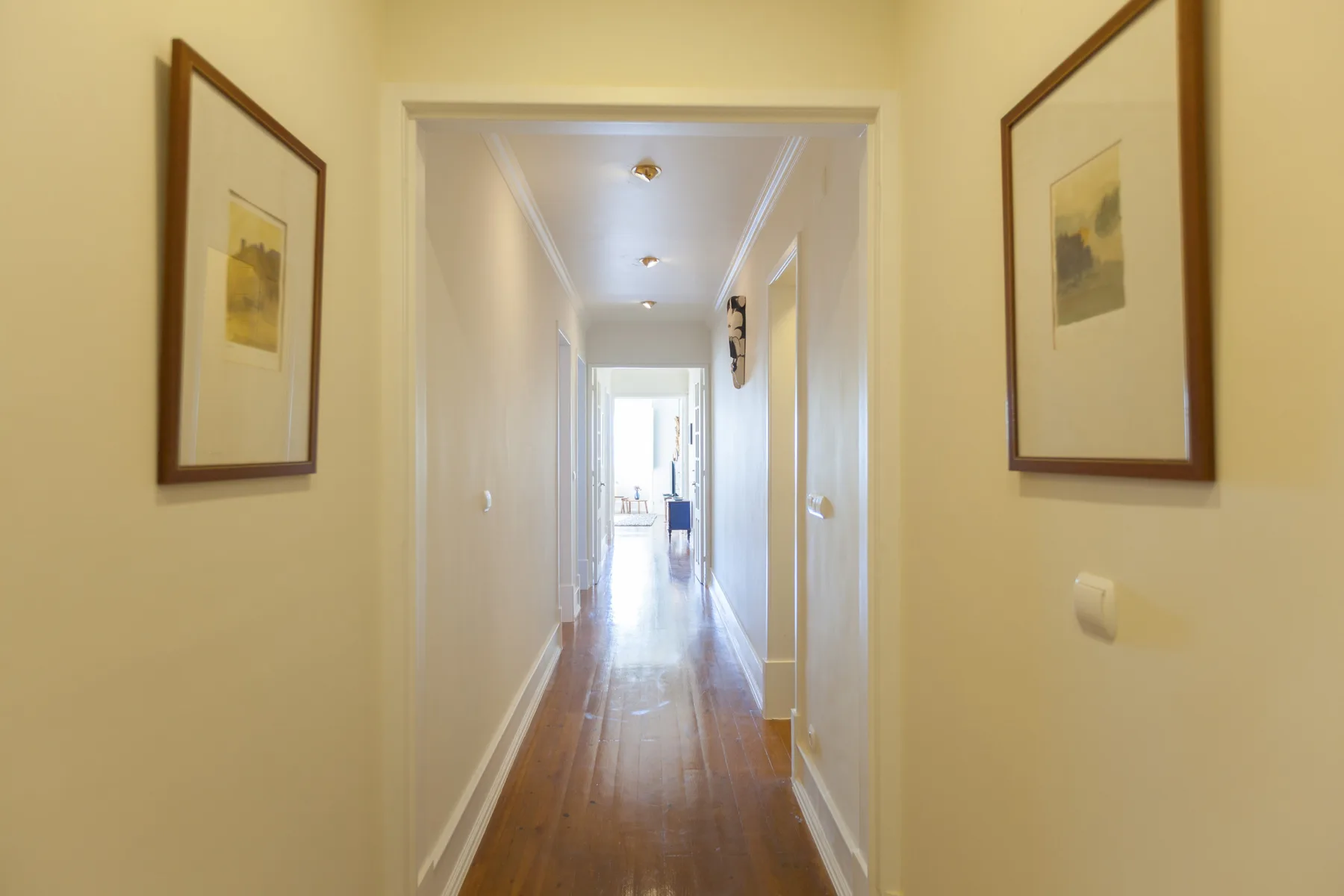 A bright hallway with framed artwork and a polished wood floor.