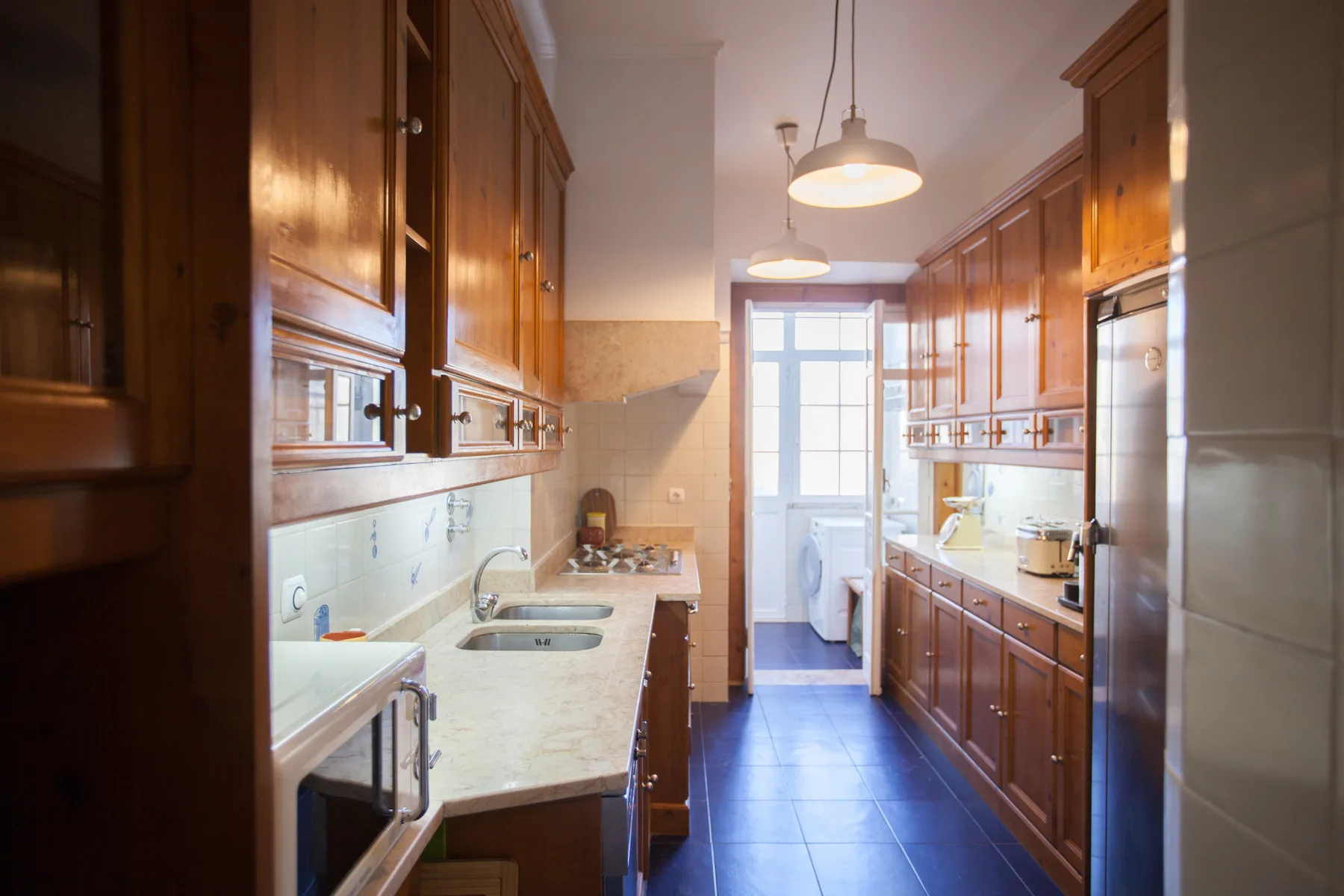 A galley kitchen with wooden cabinets and a tiled floor.