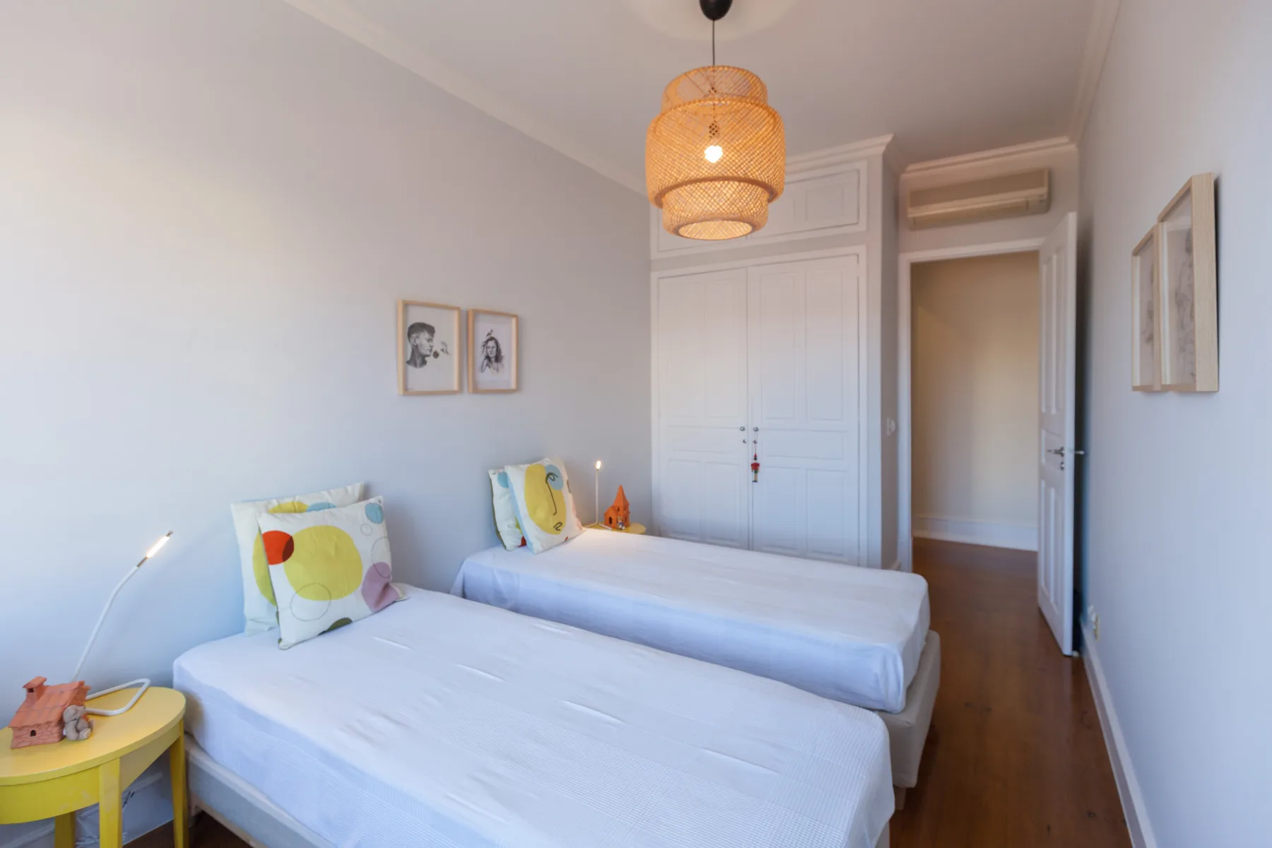 A bright bedroom with two beds, colorful pillows, and a ceiling pendant light.