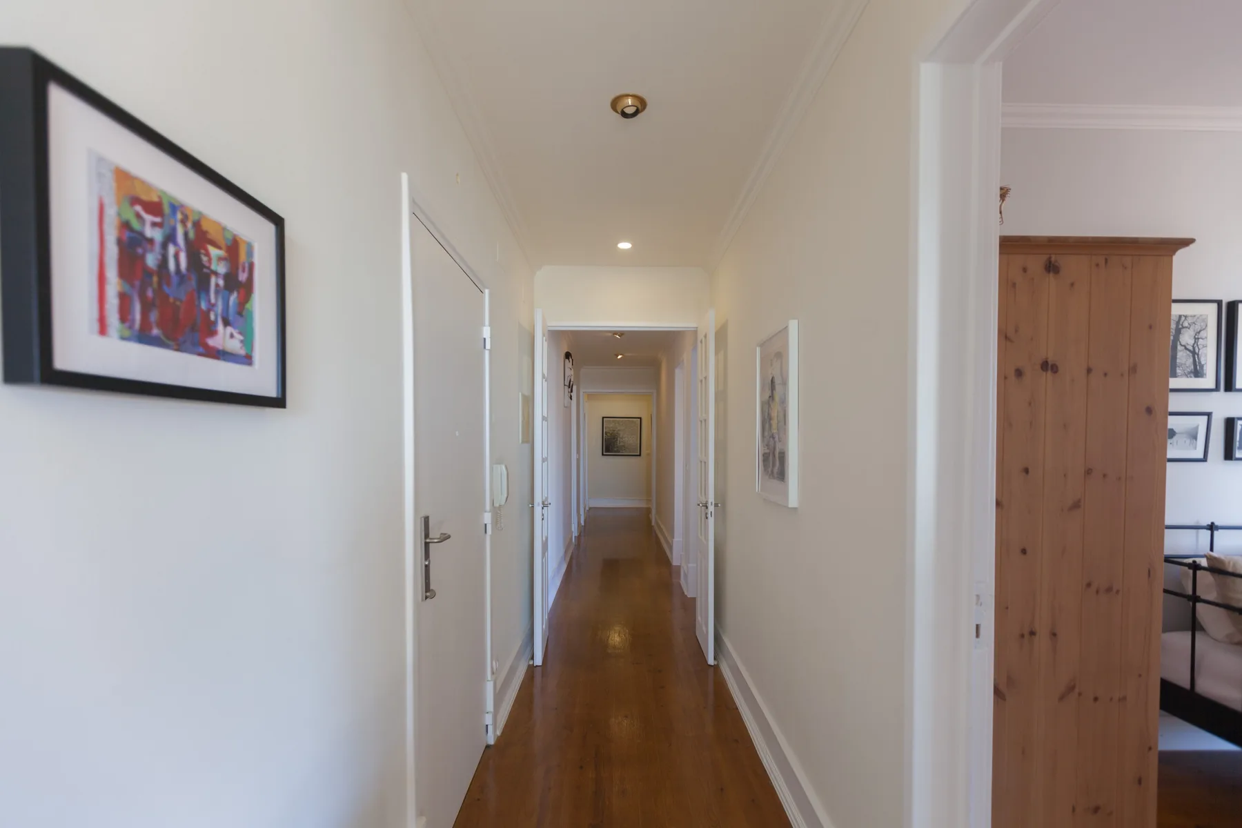 A bright hallway with wooden flooring and framed artwork on the walls.