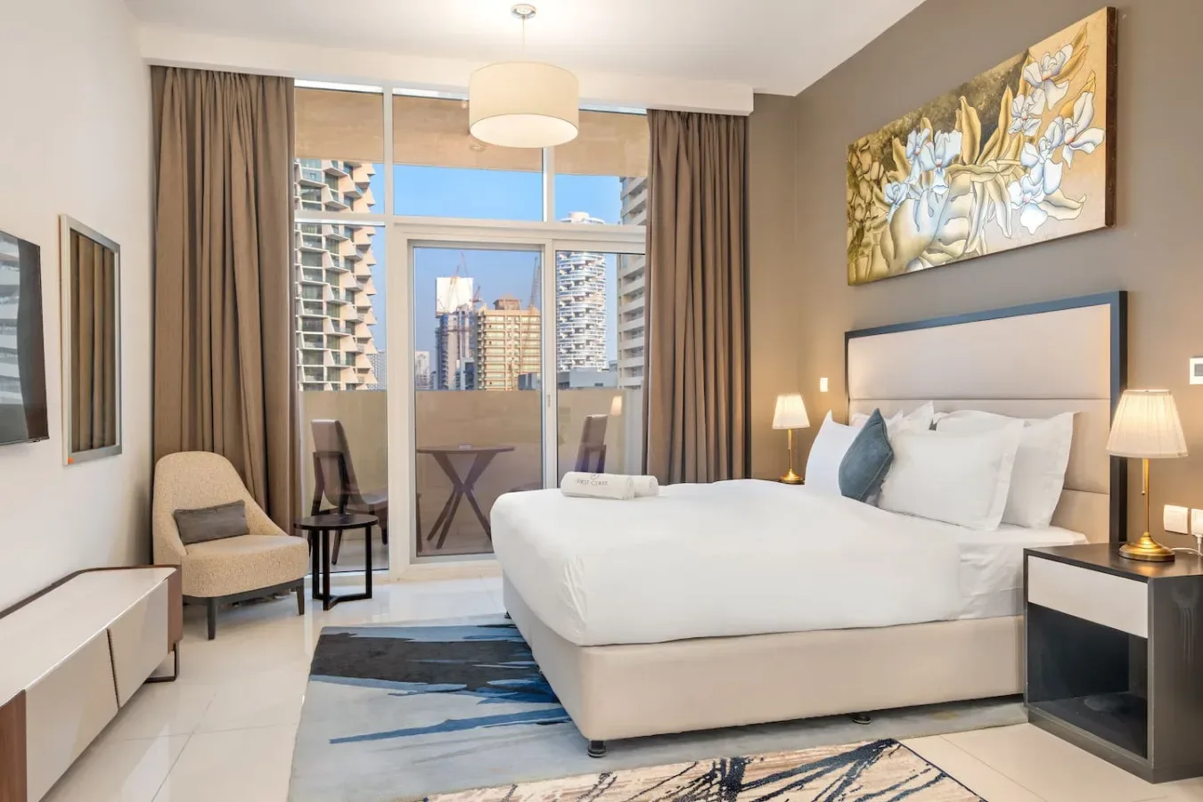 A bright bedroom with a large bed, floor-to-ceiling windows, and city buildings beyond.