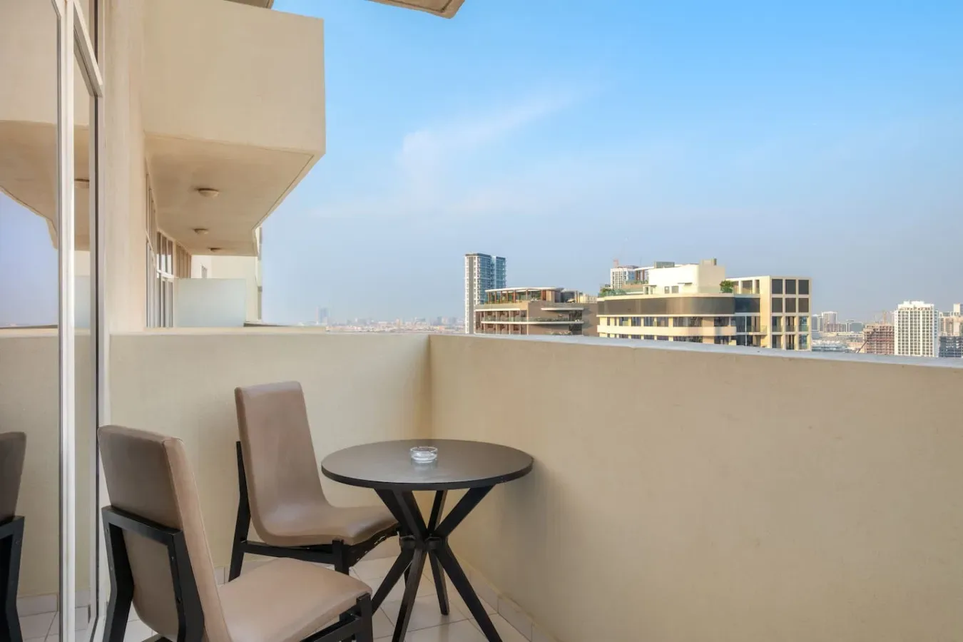 A balcony with seating and a small table overlooks nearby buildings.