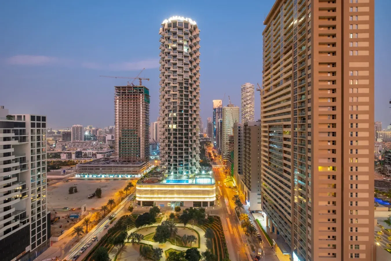 A city skyline at dusk, with illuminated high-rise buildings along the streets.