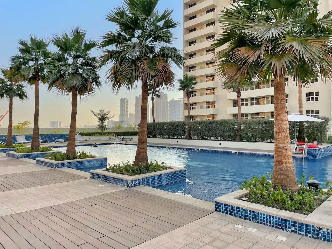 An outdoor swimming pool is surrounded by palm trees and paved decking.