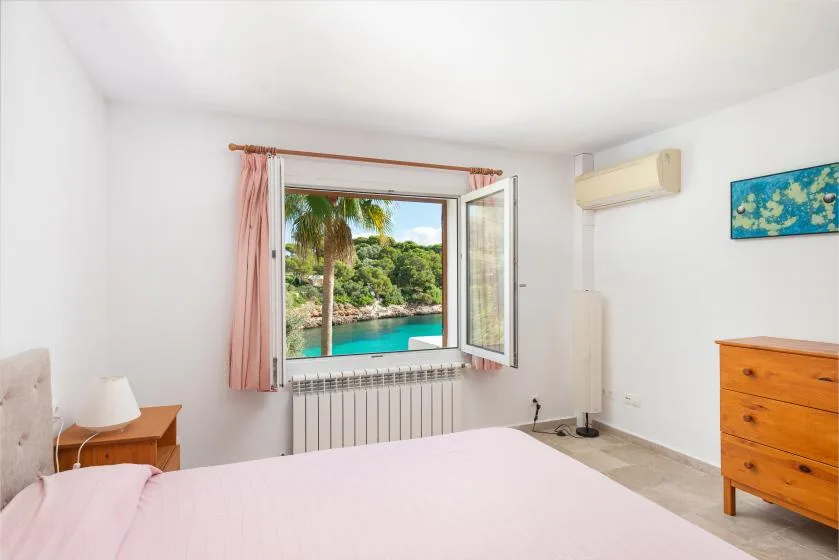 A bright bedroom with an open window overlooking greenery and water.