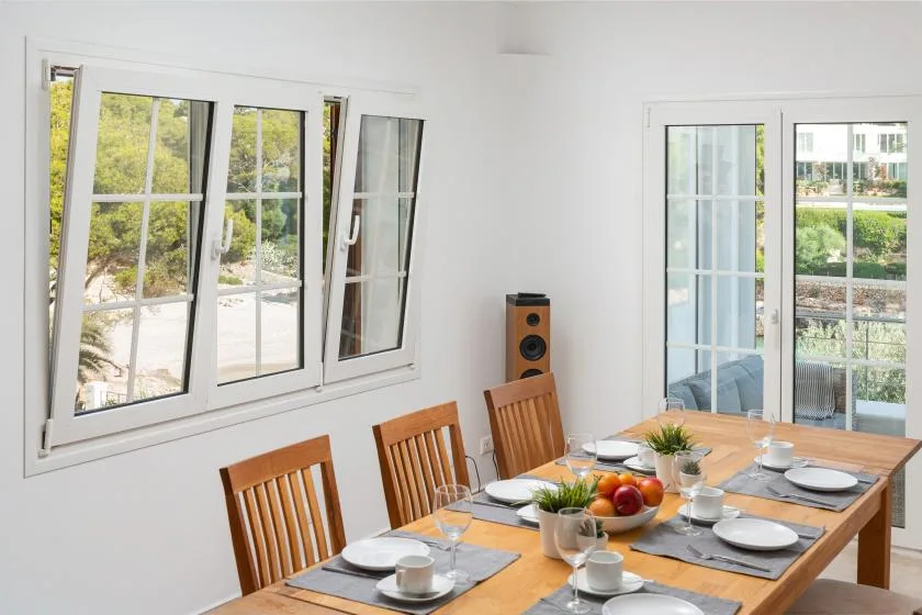 A bright dining room with a wooden table set beside large windows.