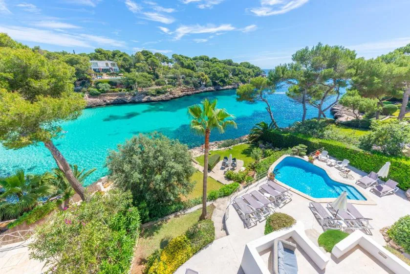 A swimming pool and landscaped gardens overlook a bright turquoise inlet.