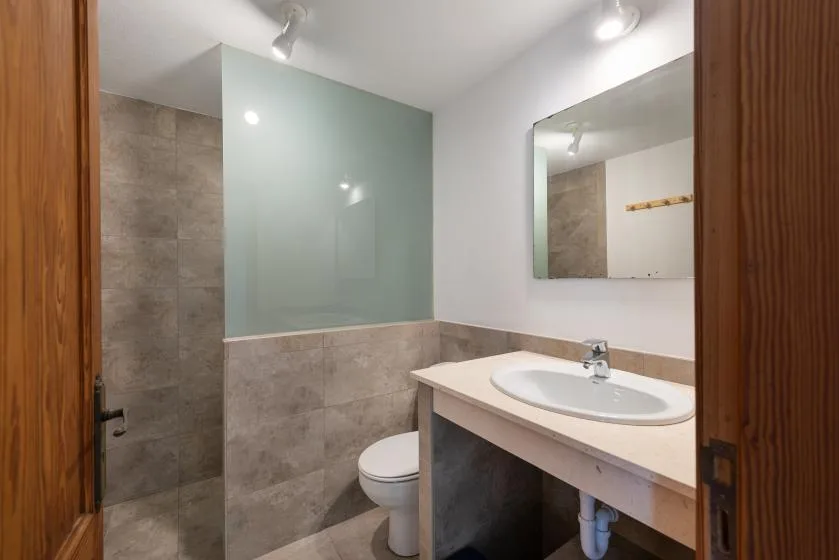 A bathroom with a sink, mirror, and glass shower screen.