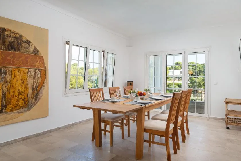 A dining room with a wooden table and chairs beside large windows.
