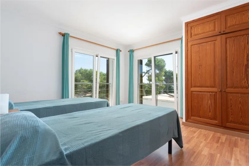 A bedroom with two beds beside large windows and a wooden wardrobe.