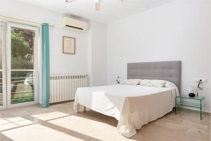 A bright bedroom with a bed beside a glass door and turquoise curtains.