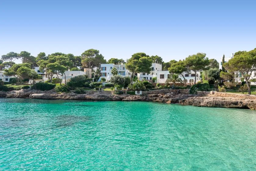 Turquoise water borders a tree-lined shore with white buildings.
