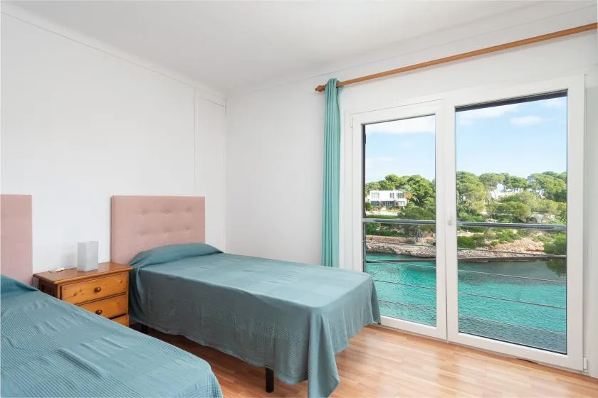 A bedroom with two beds beside large windows overlooking the water.