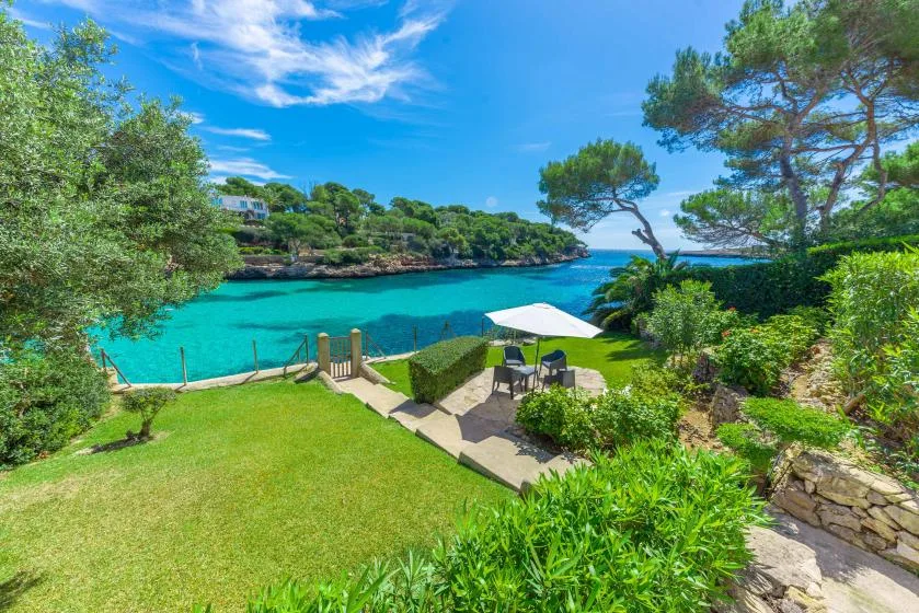 A landscaped terrace overlooks a turquoise bay, with an umbrella and seating.