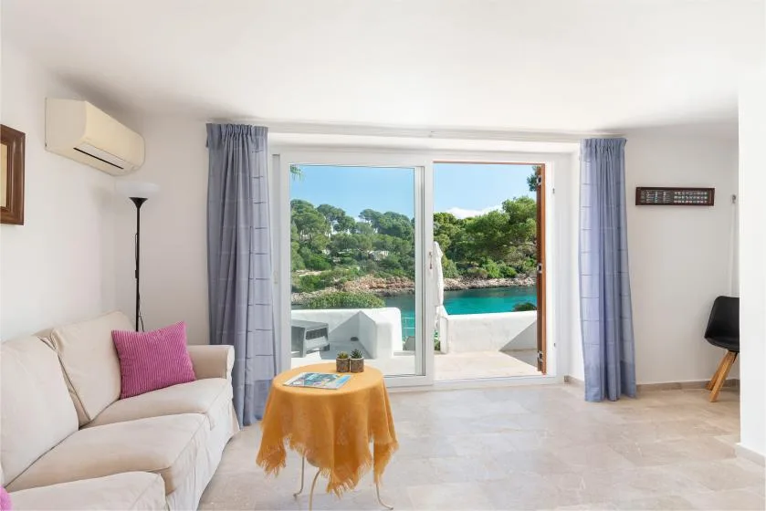 A bright living room opens onto a patio with a turquoise pool and greenery.