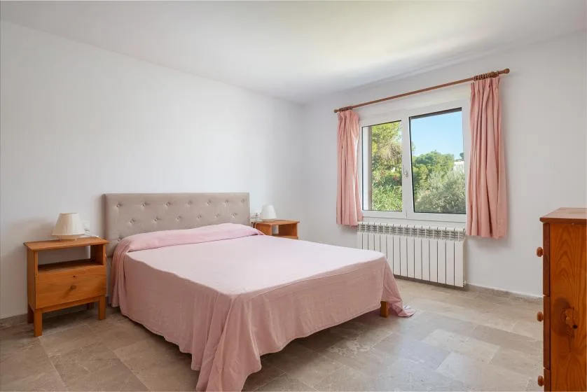 A bright bedroom with a pink bed and a window framed by curtains.