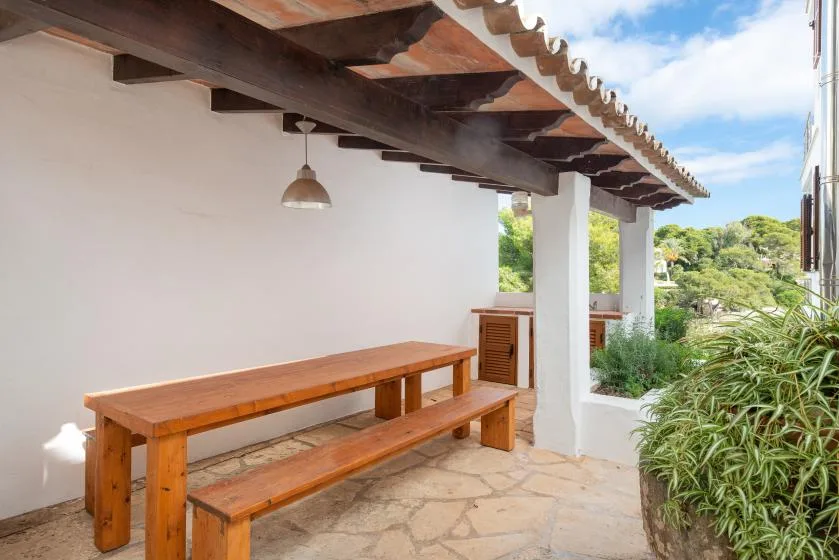 A covered outdoor patio with a long wooden table and bench beside a garden.