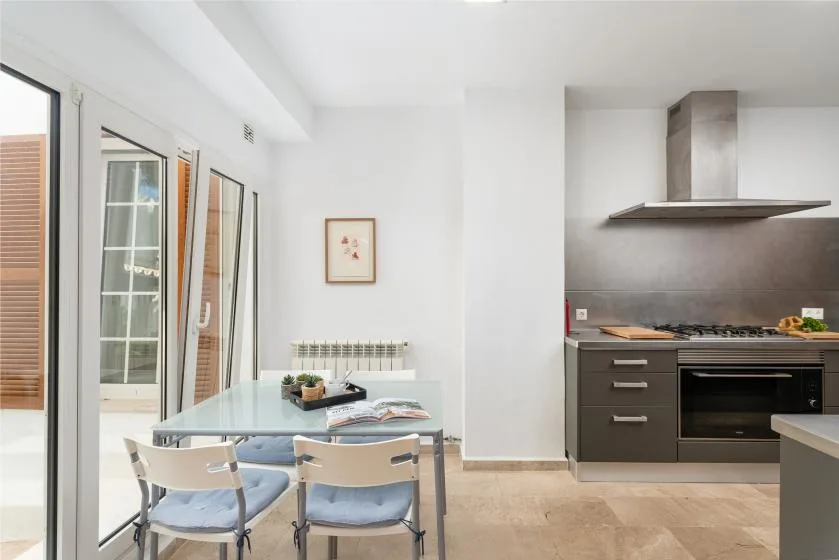 A bright dining area with a glass table beside an open kitchen.
