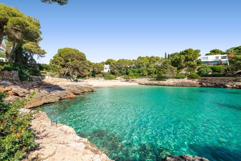 A clear turquoise bay is bordered by rocky shores and green trees.