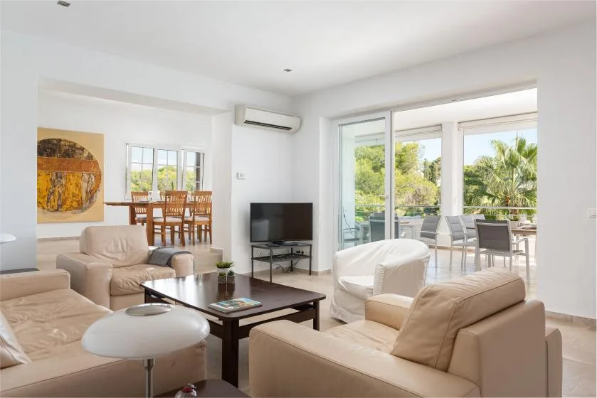 A bright living room with seating, a television, and large windows opening onto a balcony.