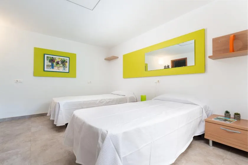 A bright bedroom with two beds and yellow-framed wall decor.