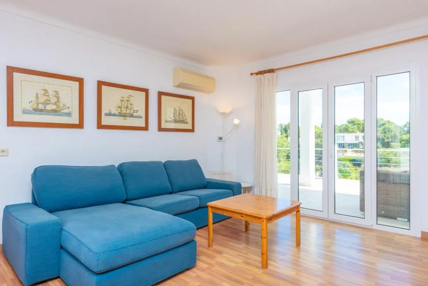 A bright living room with blue seating and tall glass doors opening onto a balcony.