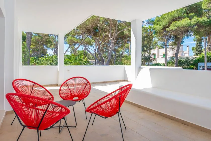 A bright enclosed seating area with red chairs beside large windows overlooking trees.