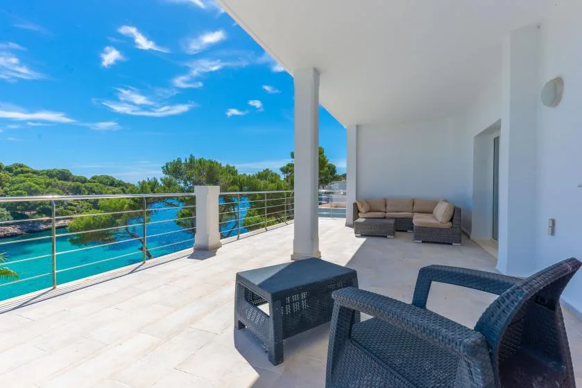 A covered terrace overlooks blue water, with outdoor seating beside the railing.