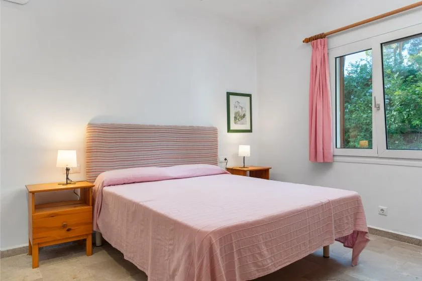 A bedroom with a bed and a window framed by pink curtains.