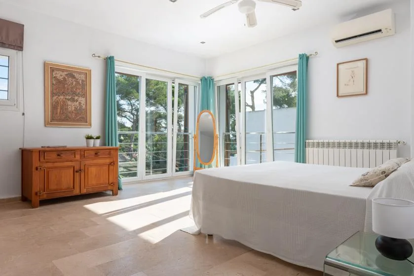 A bright bedroom with a bed beside tall windows and teal curtains.