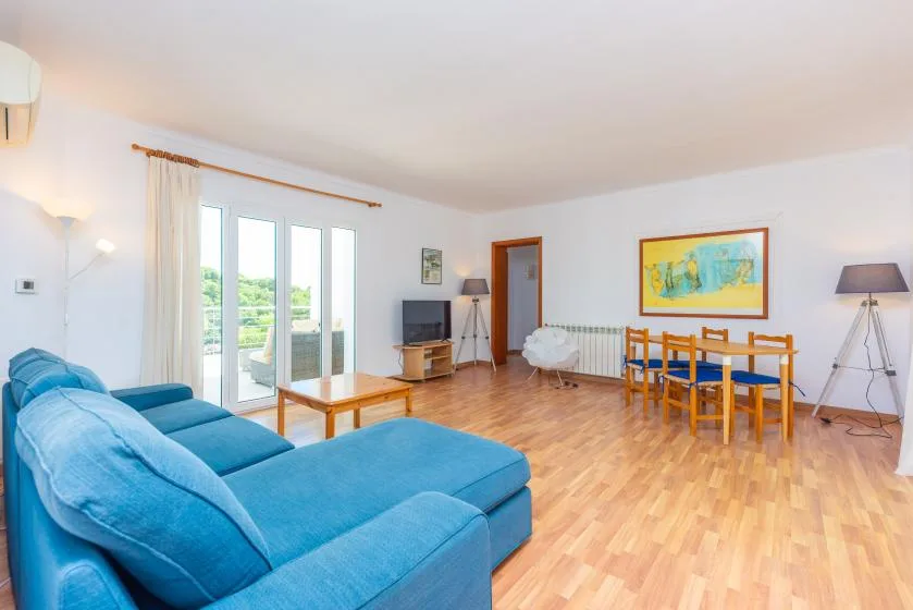 A bright living and dining area with blue seating and a wooden table.