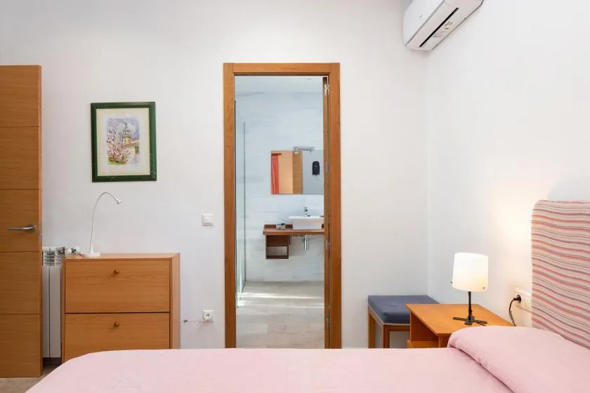 A bedroom with a bed, wooden dresser, and open doorway to a bathroom.