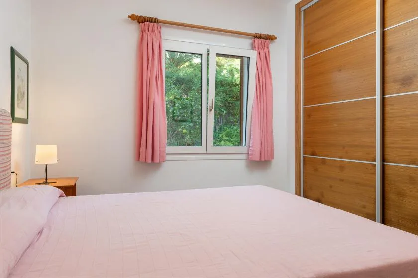 A bedroom with a bed, a window, and pink curtains.