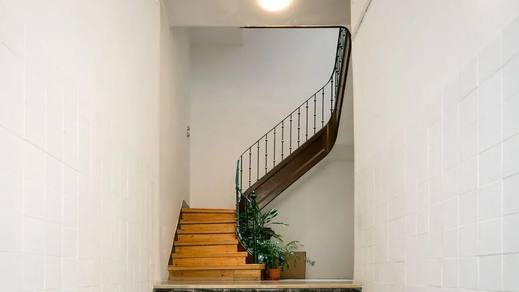 Una escalera con peldaños de madera y una barandilla metálica curva.