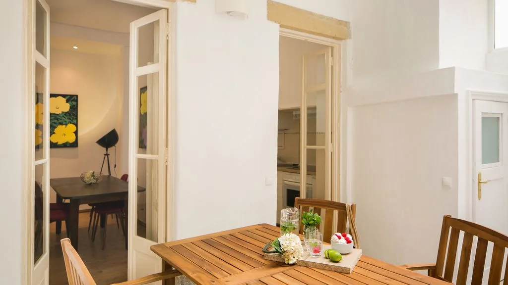 Comedor con una mesa y sillas de madera junto a puertas interiores abiertas.