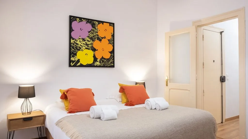 Un dormitorio con una cama bien tendida y arte floral colorido en la pared.