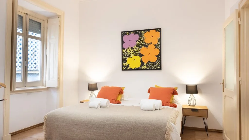 Un dormitorio con cama doble, cojines naranjas y un cuadro floral.
