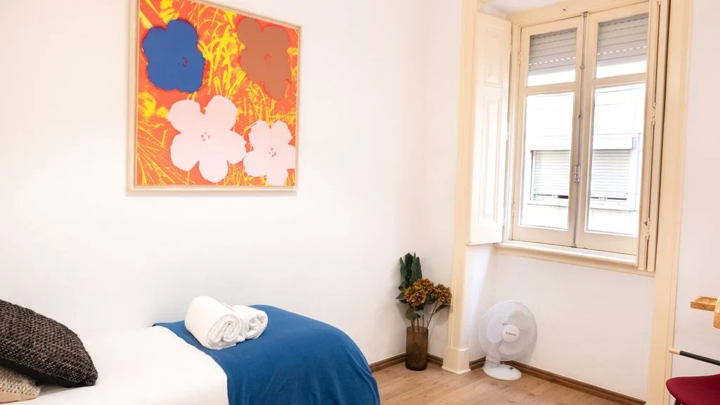 Un dormitorio con una cama, arte colorido en la pared y una ventana.