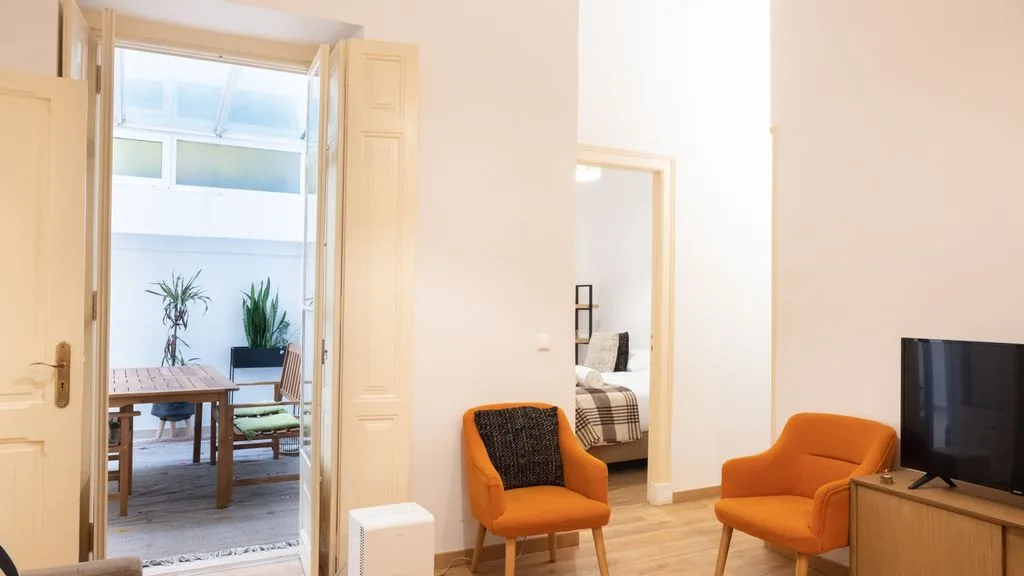 Una sala luminosa da a una terraza amueblada a través de puertas abiertas.