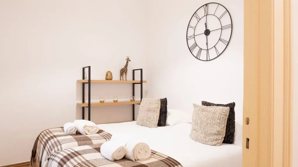 Un dormitorio con una cama, toallas dobladas y un reloj de pared.