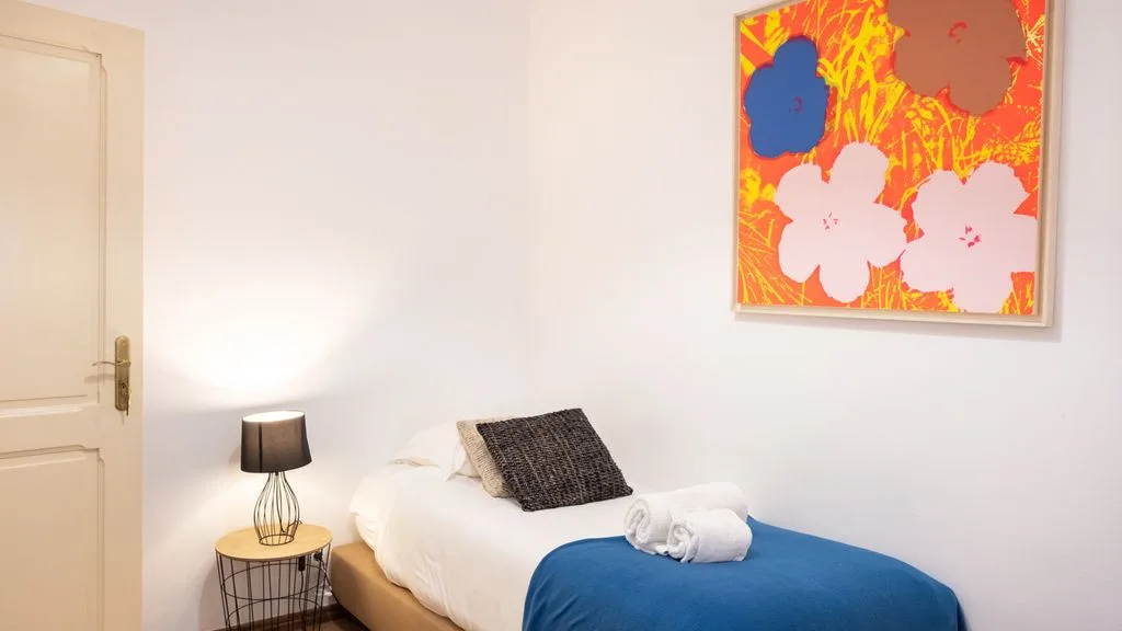 Un dormitorio con una cama bien hecha, una manta azul y arte colorido en la pared.