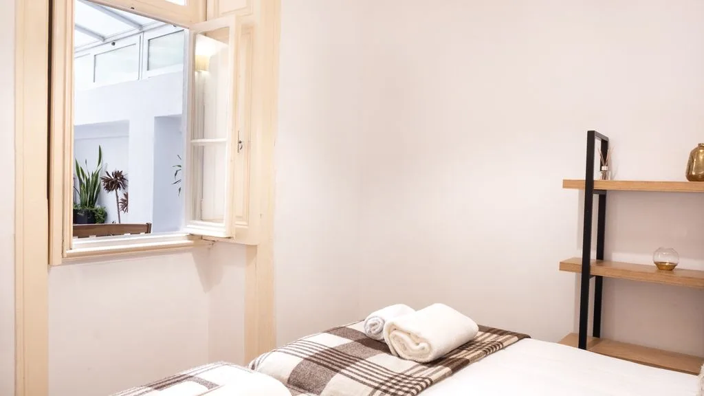 Un dormitorio con una cama bien arreglada junto a una ventana abierta.